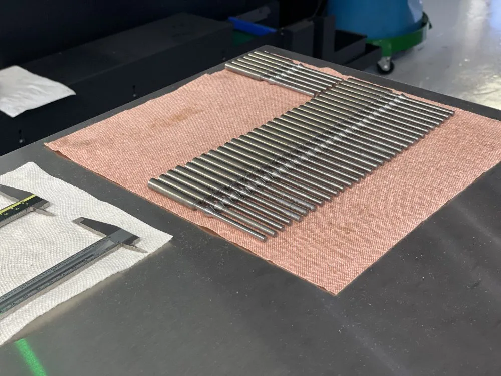 A production run of turned steel pins laid out beside calipers